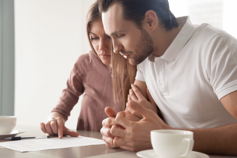 Foto van 2 personen (vrouw en man) achter een tafel die aandachtig een A4-tje lezen