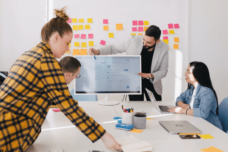 Foto van een team van mensen die kijken naar scherm met op de achtergrond een wand met post-its